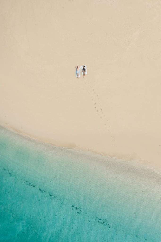 Peaceful aerial view of a beach in Zanzibar with a couple relaxing on white sand by turquoise waters.